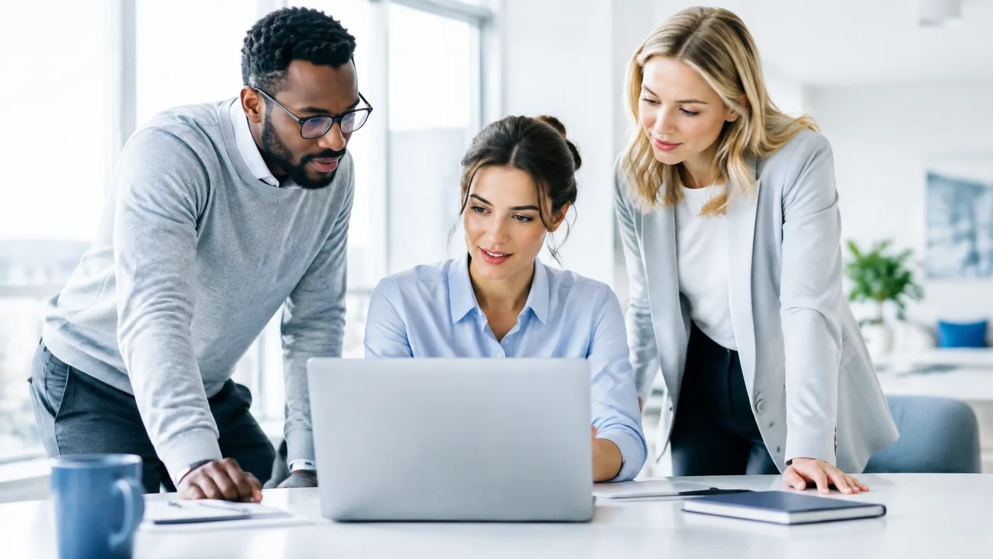 Three professionals collaborating around a laptop in a bright office
